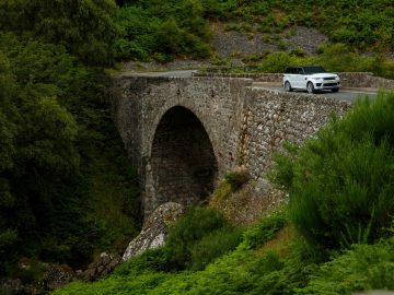 Een witte Range Rover die een oude stenen brug oversteekt, omringd door weelderig groen.