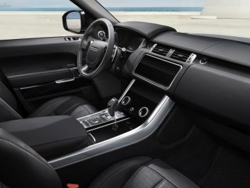 Binnenaanzicht van een moderne Range Rover met zwartleren stoelen, een middenconsole met versnellingspook en een gedetailleerd dashboard met digitale displays.