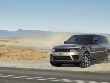 Een Range Rover rijdt op een stoffige landelijke weg met bergen op de achtergrond onder een heldere hemel.