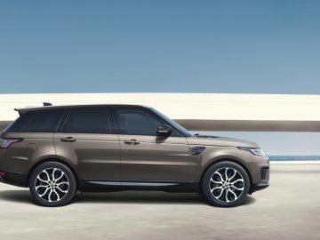 Een moderne Range Rover geparkeerd op een betonnen ondergrond met een heldere hemel op de achtergrond en een minimalistische structuur op de achtergrond.
