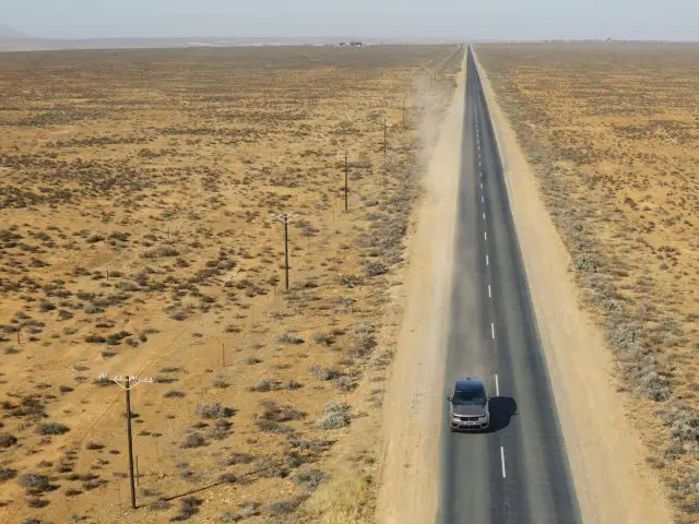 Luchtfoto van een Range Rover die over een rechte weg door een uitgestrekt, dor landschap rijdt.