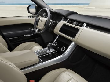 Binnenaanzicht van een Range Rover met de nadruk op beige lederen stoelen, een gedetailleerd dashboard en een strakke middenconsole met versnellingspook.