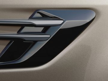 Close-up van een metalen letter 'f'-embleem op een getextureerd Range Rover-oppervlak met een verloop van lichte naar donkere tinten.
