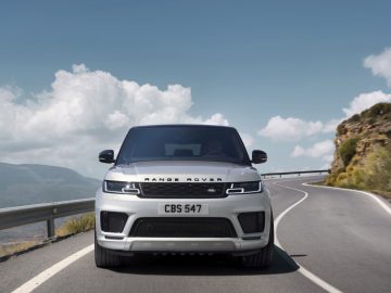 Een witte Range Rover die over een bochtige bergweg rijdt onder een helderblauwe lucht.