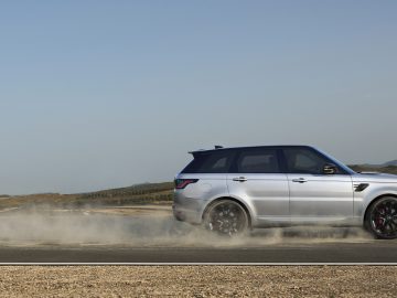 Een witte Range Rover snelt over een stoffige weg tegen een helderblauwe lucht en bergen in de verte.