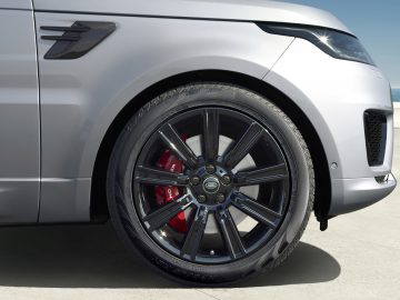 Close-up van het voorwiel en spatbord van een Range Rover, met de nadruk op een zwarte lichtmetalen velg en rode remklauw.