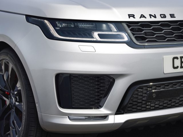 Close-up van een zilveren Range Rover-voorkant, met de nadruk op de grille en koplamp, met een zichtbare kentekenplaat.