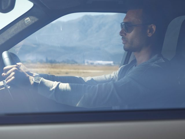 Man met zonnebril die een Range Rover bestuurt met een schilderachtig berglandschap zichtbaar door de voorruit.