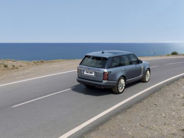 Een blauwe Range Rover die over een kustweg rijdt met de oceaan op de achtergrond.