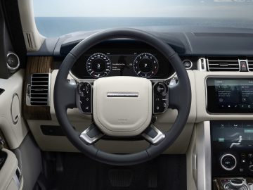 Binnenaanzicht van het dashboard en het stuur van een moderne Range Rover met digitale displays en lederen afwerking.