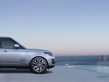 Een zilveren Range Rover geparkeerd op een dak met glazen randen met uitzicht op de oceaan tijdens de schemering.