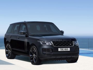 Een zwarte Range Rover geparkeerd op een terras aan zee met een helderblauwe lucht en de oceaan op de achtergrond.