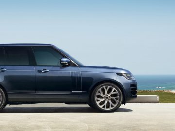 Een blauwe Range Rover geparkeerd buiten een modern huis vlakbij de kust op een zonnige dag.