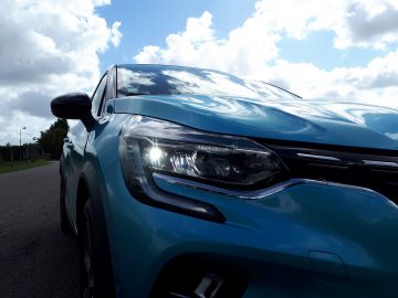 Blauwe E-Tech-auto met koplampen aan, weergegeven vanuit een lage hoek met een bewolkte lucht op de achtergrond.