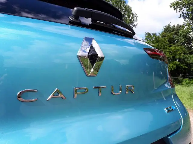 Close-up van het logo aan de achterkant en de modelnaam op een blauwe Renault Captur E-Tech-auto.