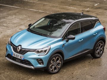 Een blauwe Renault Captur E-Tech geparkeerd op een nat grindoppervlak.