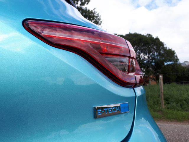 Close-up van de achterkant van een Renault Clio met de nadruk op de blauwe verf en het 'E-Tech Hybrid'-embleem onder het achterlicht.