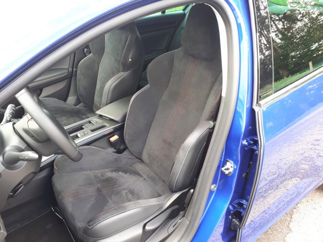 Binnenaanzicht van de Mégane E-Tech met de bestuurdersstoel en het dashboard, de deur open, met de nadruk op het blauwe exterieur en de stoffen stoelen.