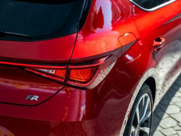 Close-up van de achterkant van een rode Seat Leon, met een deel van het achterlicht en het FR-embleem.