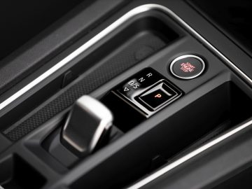 Close-up van de automatische versnellingspook van een Seat Leon met rij-, achteruit- en parkeeropties zichtbaar op een glanzend zwarte console.