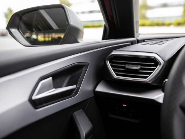 Close-up van het interieur van een Seat Leon met de zijkant van het dashboard, de ventilatieopening en de deurgreep met de nadruk op details en texturen.