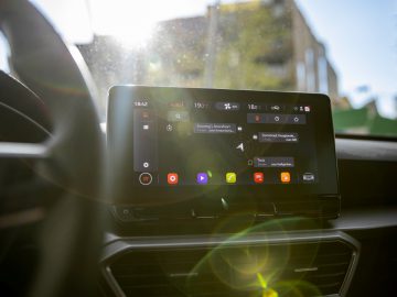Het infotainmentsysteem van een Seat Leon met kleurrijke app-pictogrammen, bekeken vanaf de bestuurdersstoel terwijl het zonlicht op het scherm schijnt.
