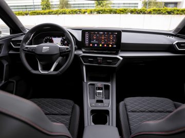 Binnenaanzicht van een Seat Leon, met de nadruk op het stuur, het dashboard met digitale displays en lederen stoelen.