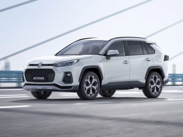 Een witte Suzuki Across SUV die over een brug rijdt met een onscherpe achtergrond, die beweging overbrengt.