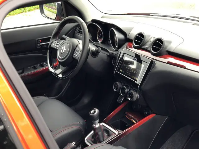 Interieur van een Suzuki Swift Sport met een stuur met logo, dashboard met ronde ventilatieopeningen, handmatige versnellingspook en een touchscreen.