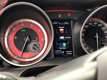 Suzuki Swift Sport-dashboard met een toerenteller, motortemperatuur en hybridesysteemstatus met brandstofmeter en batterijniveau.