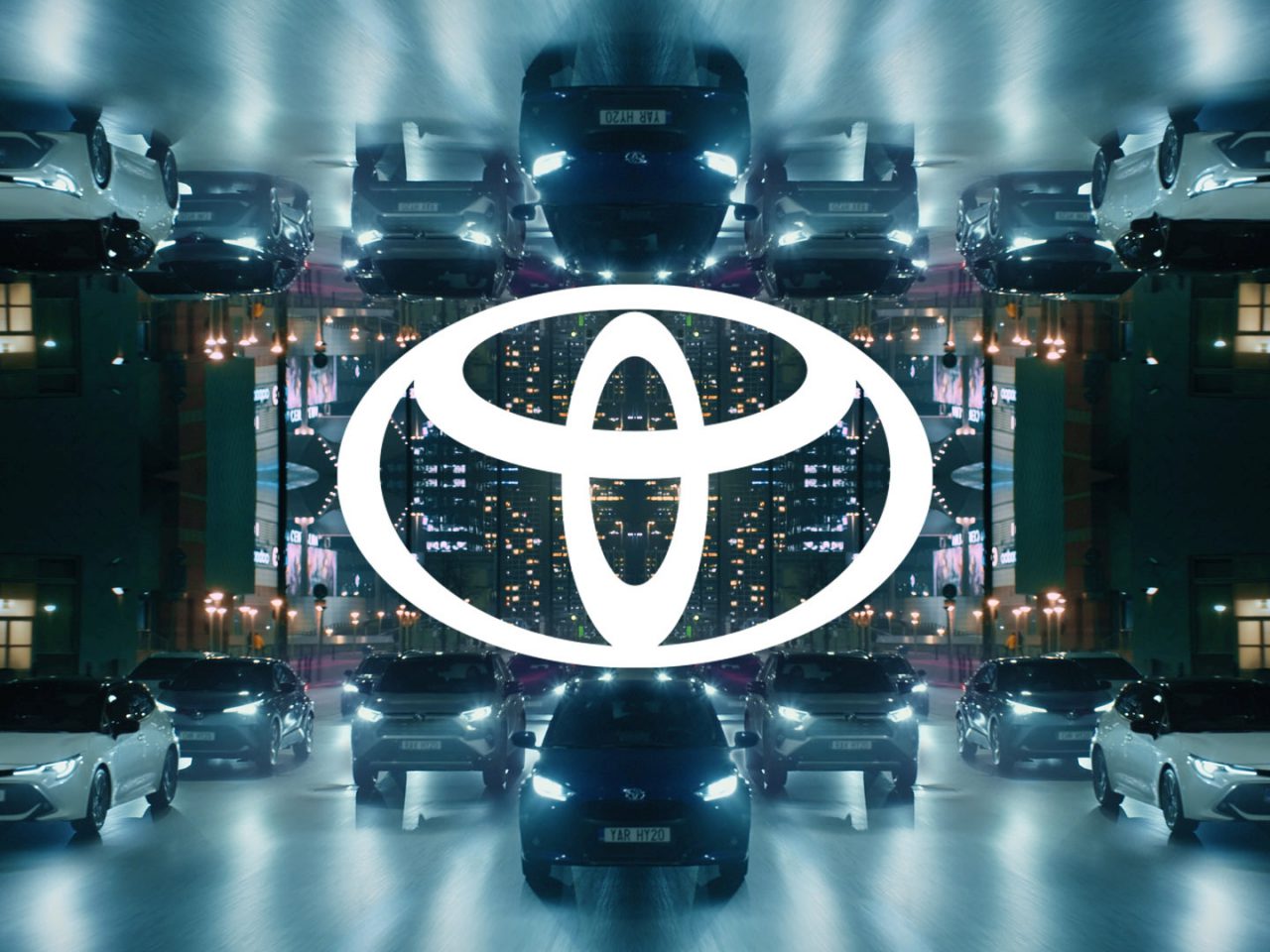 Symmetrisch beeld van verschillende Toyota-voertuigen en het Toyota-logo gecentreerd, met 's nachts een gespiegelde stadsachtergrond.