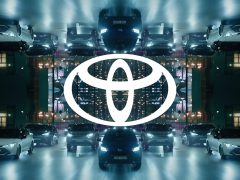Symmetrisch beeld van verschillende Toyota-voertuigen en het Toyota-logo gecentreerd, met 's nachts een gespiegelde stadsachtergrond.