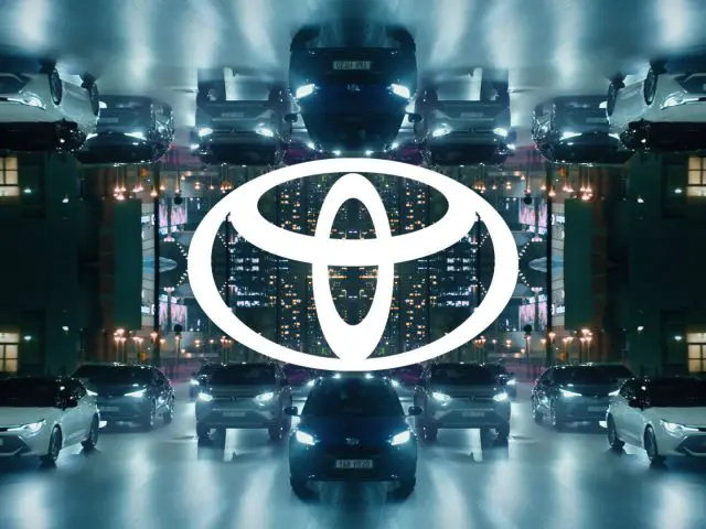 Symmetrisch beeld van verschillende Toyota-voertuigen en het Toyota-logo gecentreerd, met 's nachts een gespiegelde stadsachtergrond.