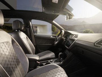 Luxe Volkswagen Tiguan-interieur met modern dashboard en panoramisch schuifdak met uitzicht op schilderachtige bergen.