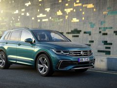 Een blauwe Volkswagen Tiguan SUV geparkeerd voor een moderne muur met vierkante patronen tijdens het gouden uur.