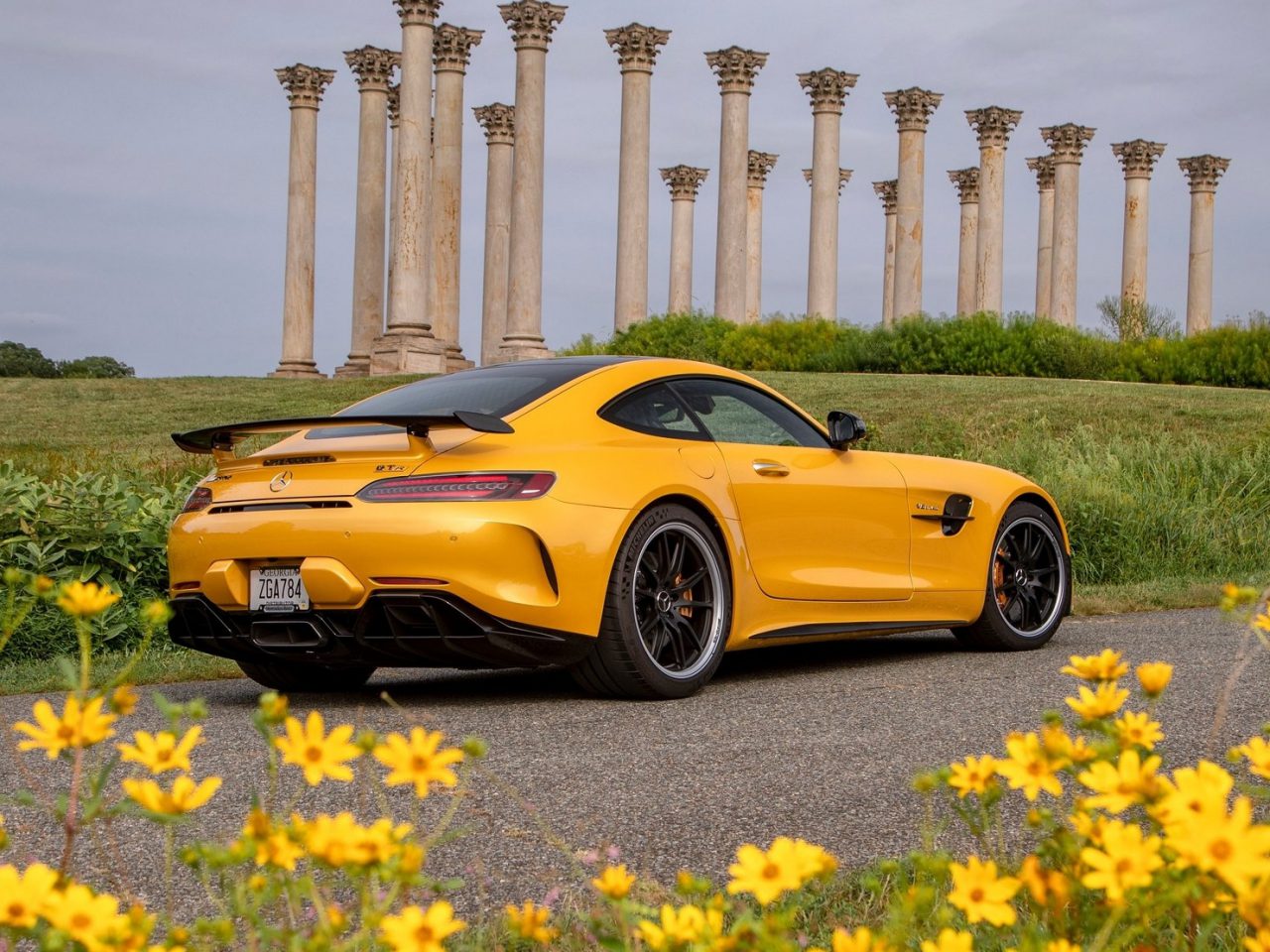 Felgele droomauto geparkeerd in een grasveld met een rij klassieke zuilen op de achtergrond.