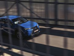 Een Lexus UX 300e SUV die snel over een brug rijdt met wazig bewegingseffect, waarbij snelheid en dynamische bewegingen worden benadrukt.