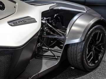 Close-up van het achterwiel en de koolstofvezelcarrosserie van een Ariel Atom-sportwagen, met gedetailleerde ophanging en innovatief ontwerp.