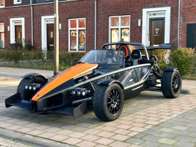 Een Ariel Atom-sportwagen, zwart en oranje van kleur, geparkeerd in een woonstraat voor bakstenen huizen.