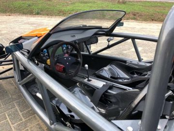 Binnenaanzicht van een Ariel Atom-sportwagen met een stuurwiel, dashboard en koolstofvezeldetails.