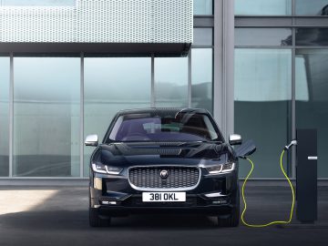 Een elektrische SUV van Jaguar laadt op bij een station voor een modern gebouw, met een gedeeltelijk bewolkte hemel boven zijn hoofd.
