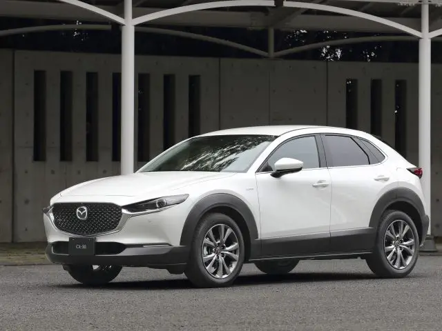 Witte Mazda CX-30 die buiten geparkeerd staat en zijn gestroomlijnde ontwerp met sportieve rondingen onder bewolkte verlichting laat zien.