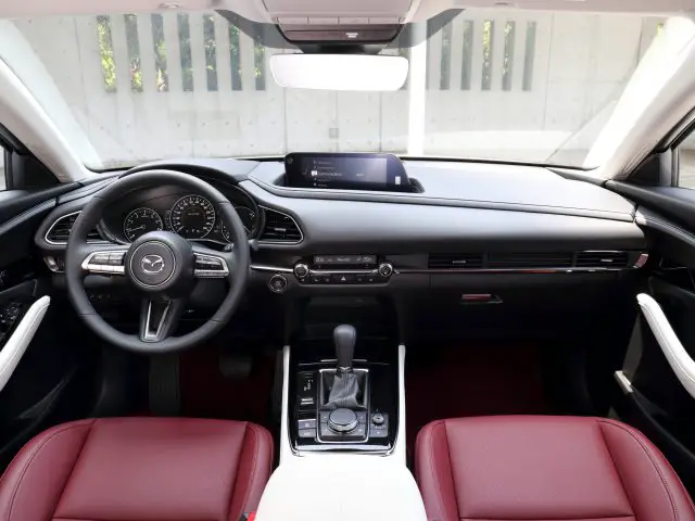 Binnenaanzicht van een Mazda CX-30 met een zwart dashboard, stuur en rood lederen stoelen.