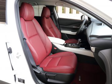 Interieur van een Mazda CX-30 met roodleren stoelen, open bestuurdersdeur en een witte buitenkant.