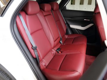 Luxe auto-interieur van een Mazda CX-30, met uitzicht op roodleren achterbanken met veiligheidsgordels en een open deur.