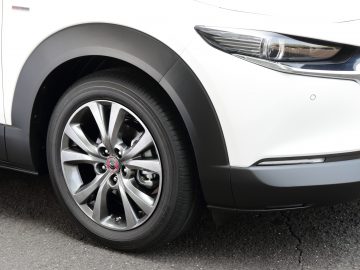 Close-up van het voorwiel van een Mazda CX-30, met een gedetailleerde lichtmetalen velg en een zichtbaar merklogo op de wieldop.