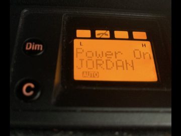 Digitaal display met daarop 'power: on Michael Jordan' met verlicht batterijpictogram, gehuisvest in een zwart paneel met dim- en autoknoppen.