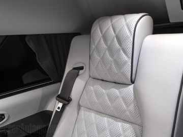 Wit lederen Cadillac autostoeltje met ruitpatroon stiksel en veiligheidsgordel, geplaatst bij een getinte autoruit.