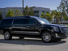 Zwarte, op maat gemaakte Cadillac Escalade SUV, buiten geparkeerd op een zonnige dag, met chromen wielen en getinte ramen.