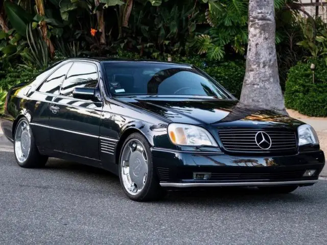 Een klassieke Mercedes-coupé geparkeerd op straat, met glanzende chromen velgen en reflecterende palmbomen.